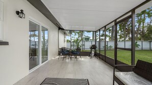 A covered patio area with a table and chairs, a bench, and large windows offering a view of the outdoors. - 3BR Home • River Access • Boating • Screened Lanai (Fort Myers)