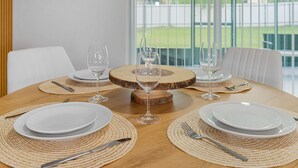 A dining table set with white plates, cutlery, and wine glasses, surrounded by woven placemats and a central wooden board. - 3BR Home • River Access • Boating • Screened Lanai (Fort Myers)