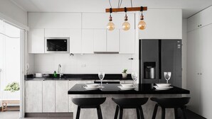 A modern kitchen with a central island, black bar stools, a microwave, a refrigerator, and hanging pendant lights. - Charming 3-bedroom apartment with rooftop pool in Barranco (Barranco)