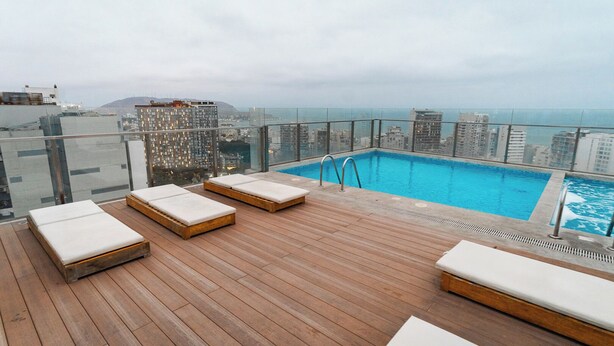 A rooftop pool area with wooden deck and lounge chairs, overlooking a cityscape and the ocean. - Charming 3-bedroom apartment with rooftop pool in Barranco (Barranco)