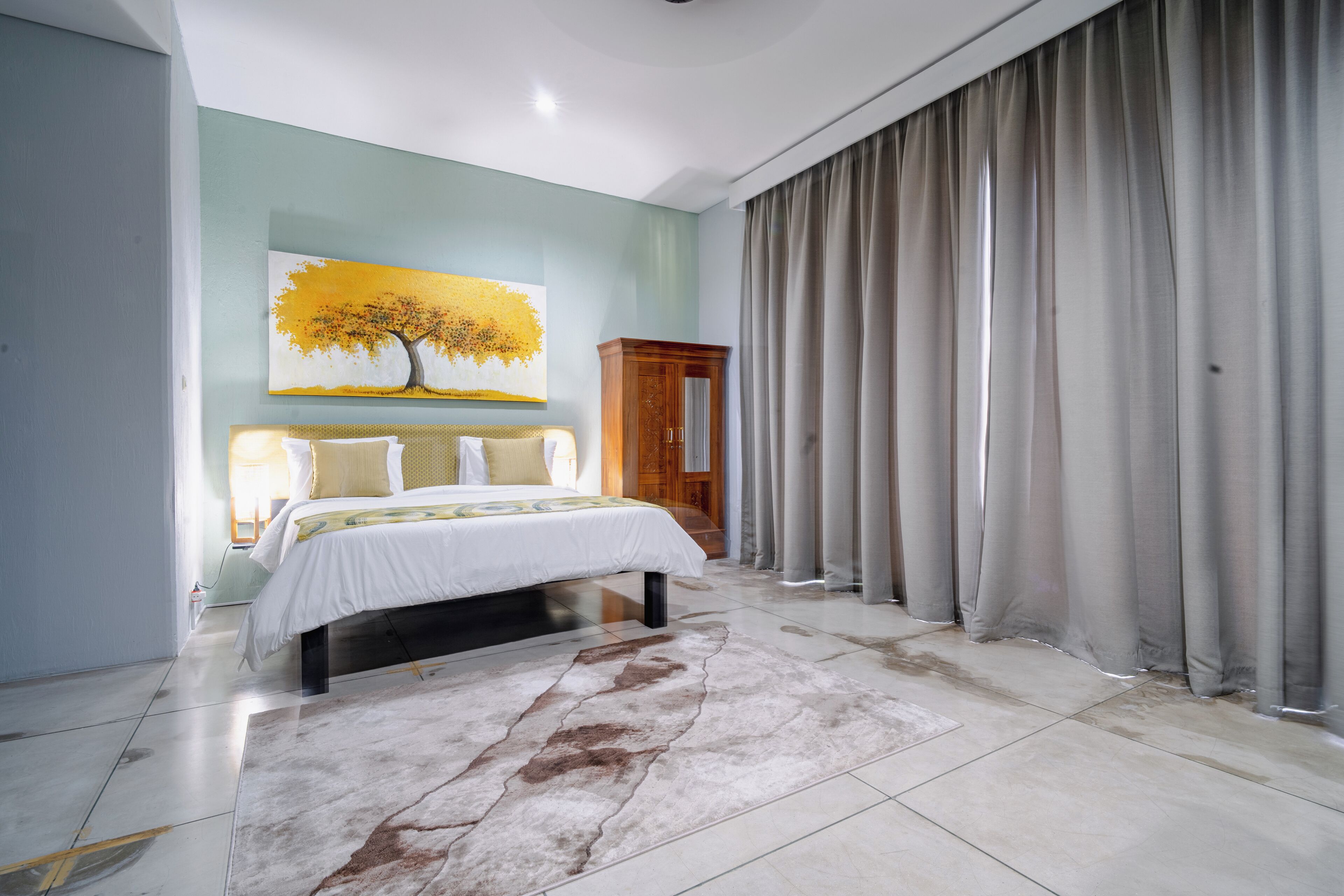 A bedroom with a bed, a large painting, a wooden wardrobe, and a curtain.