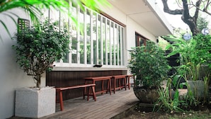 A wooden deck with benches, a potted plant, and a window overlooking greenery. - Jimbaran Beach Bliss Villa Bali (Kedonganan)