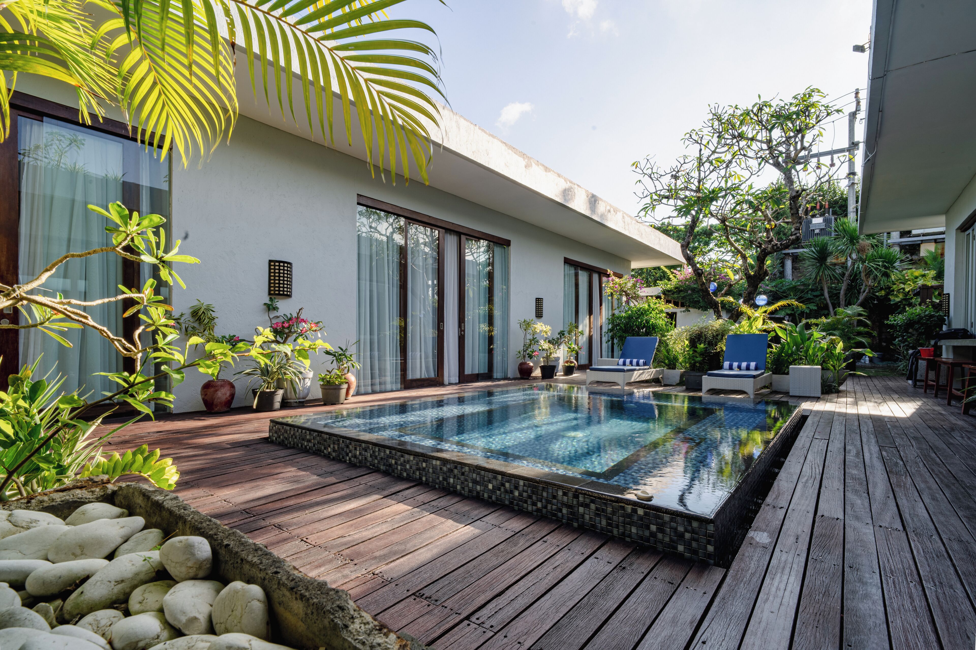 Una piscina con cubierta de madera, rodeada de plantas en macetas y una casa moderna.
