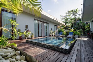 Een zwembad met houten terras, omringd door potplanten en een modern huis.