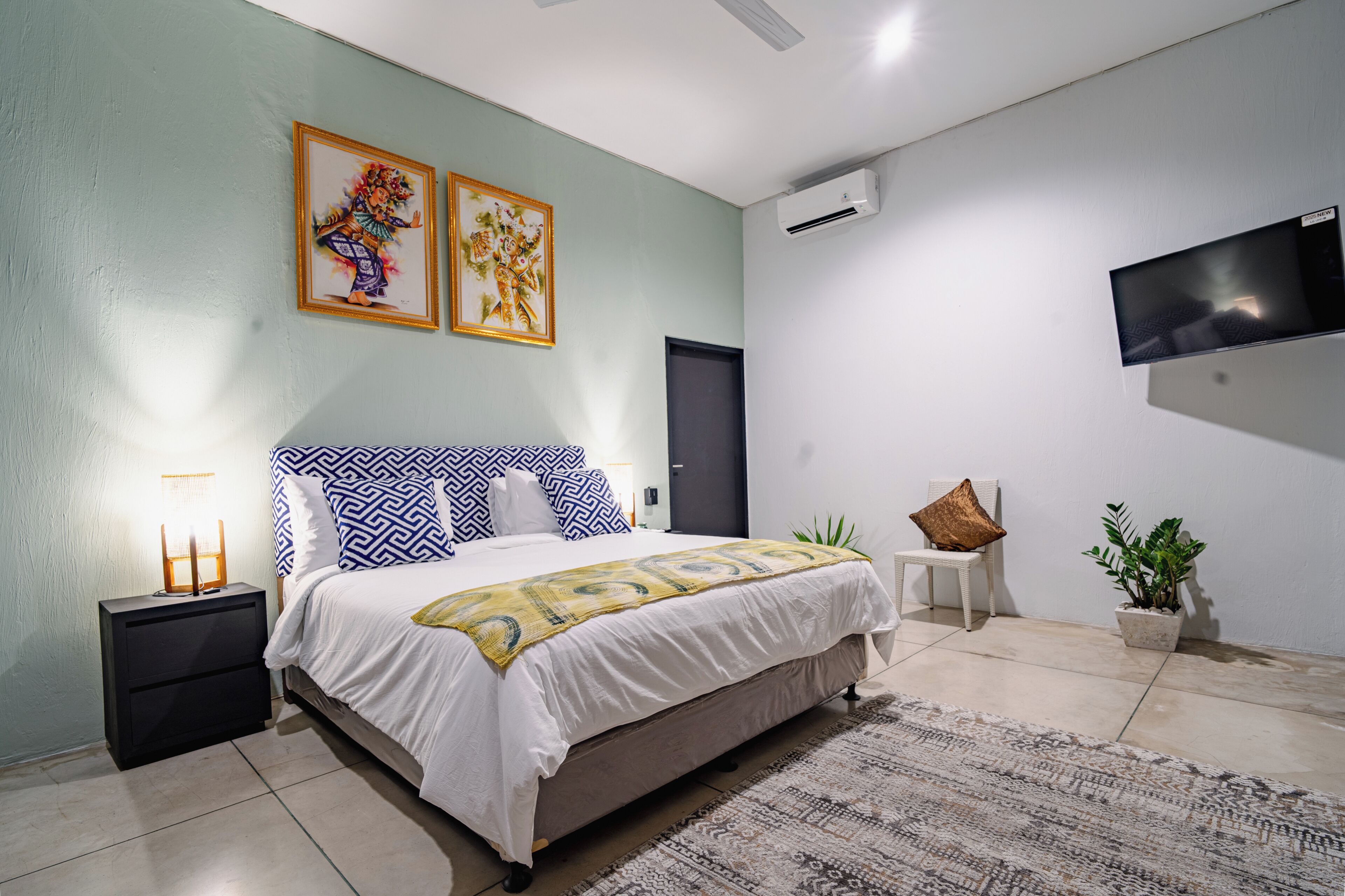 A bedroom with a bed, bedside tables, a TV, a door, and a potted plant.