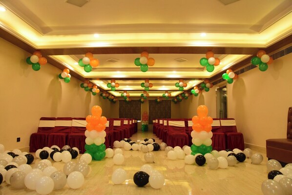 Un salón de conferencias con filas de mesas y sillas, decorado con globos y cubierto con manteles rojos.