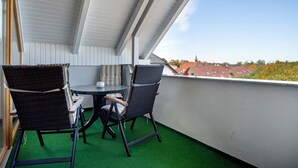 En balkon med to fletstole og et lille bord, gulv af grøn kunstgræs og udsigt til bygninger i det fjerne.