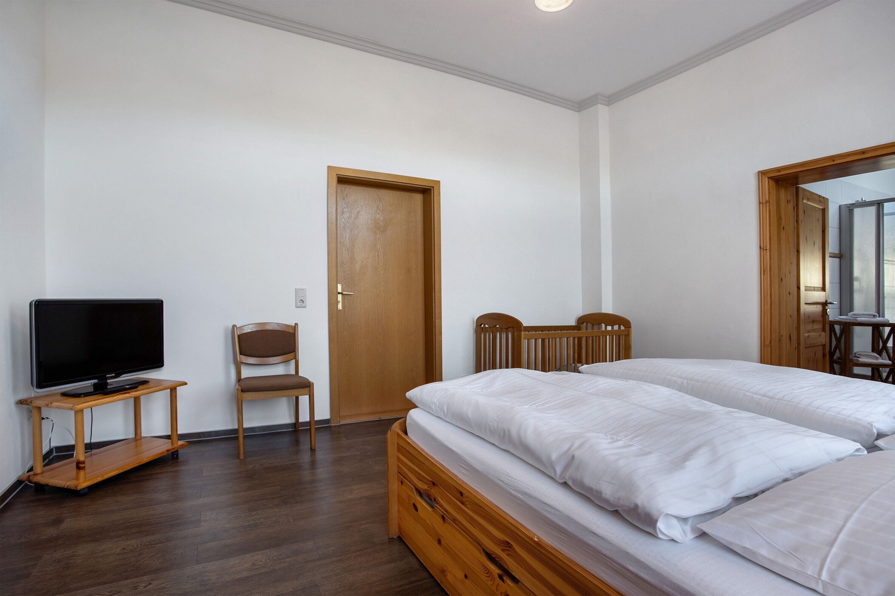 Ein Schlafzimmer mit einem Holzbett, einem Fernseher auf einem Holzständer, einem Sessel und einer Tür.
