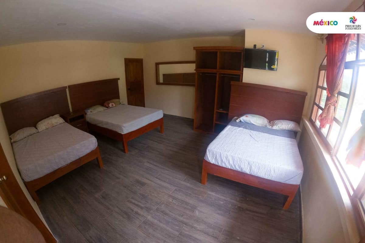 Hotellihuone, jossa on kolme puista sänkyä, vaatekaappi ja seinälle asennettu televisio.
