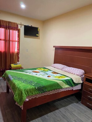 A bedroom with a wooden bed, green floral bedspread, and a wooden nightstand.