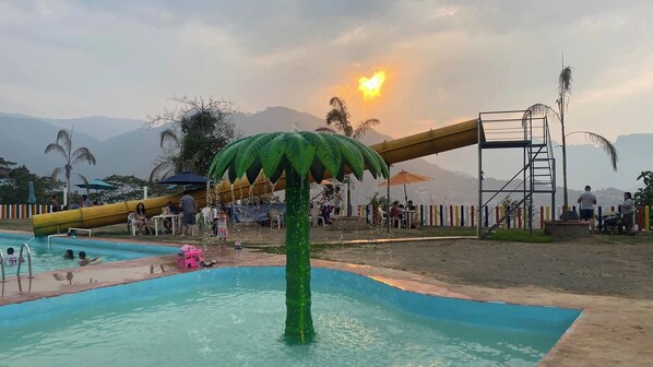 A water park with a slide, a pool, and a large palm tree structure.
