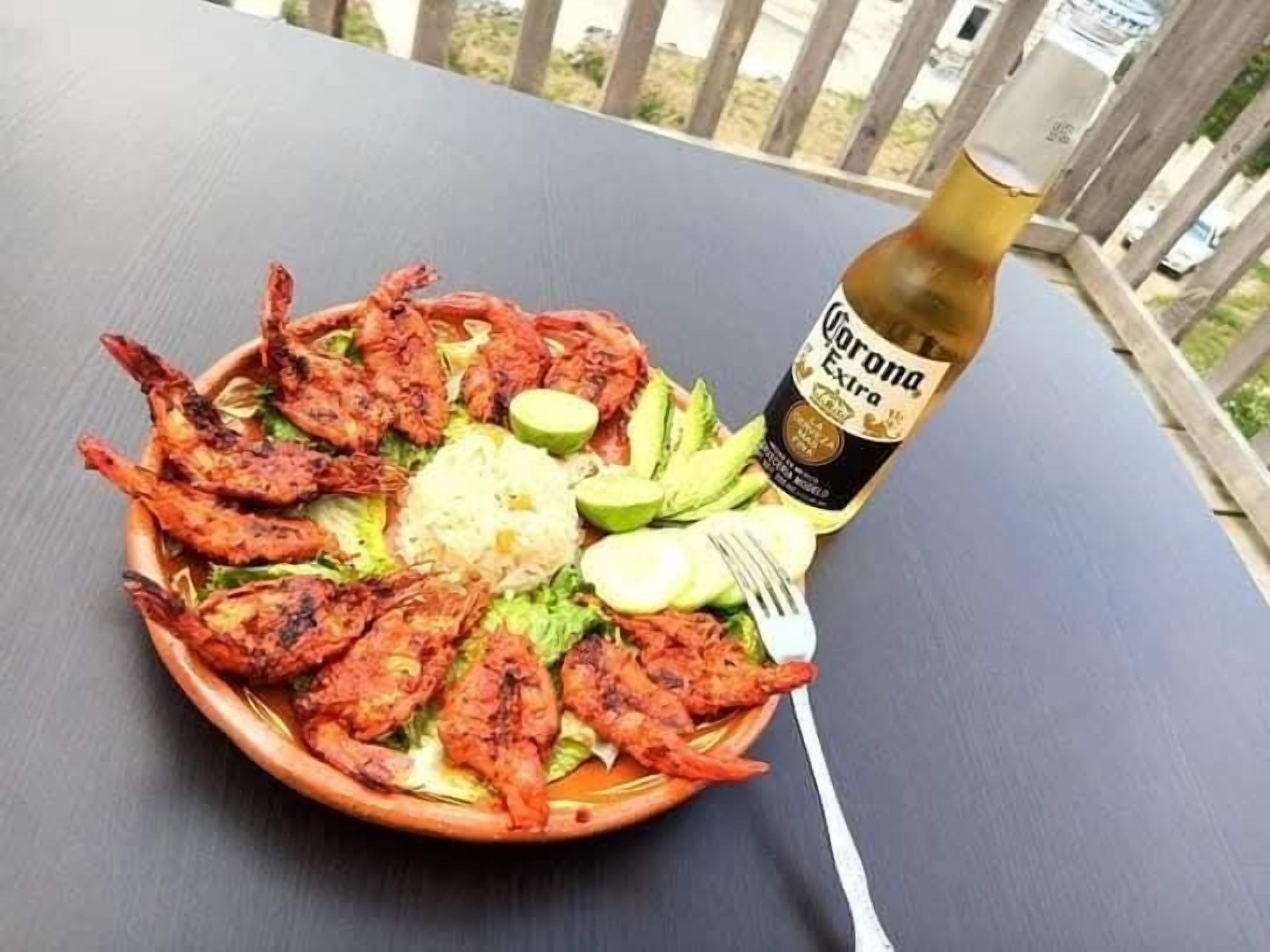 Prato com camarões grelhados, arroz e abacate sobre uma mesa com uma garrafa de cerveja Corona Extra.