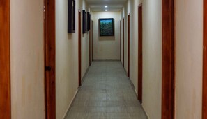 Un pasillo con puertas de madera a ambos lados, suelo de baldosas y un cuadro en la pared.
