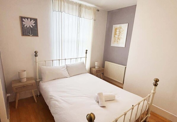 Un dormitorio con cama, mesitas de noche, un radiador y una ventana con cortinas.