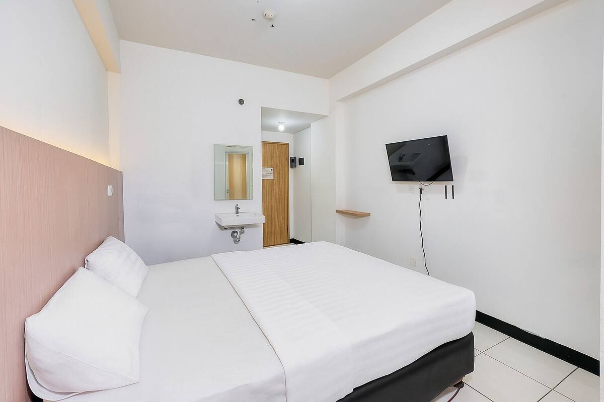 A hotel room with a bed, a TV mounted on the wall, a sink, and a mirror.