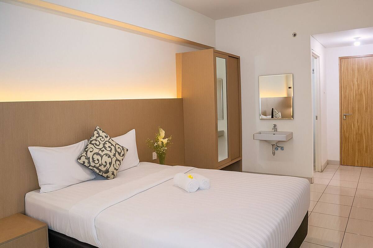 A hotel room with a bed, a bedside table, a mirror, a sink, and a door.