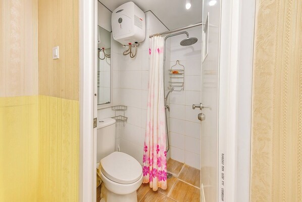 A bathroom with a toilet, shower, and a towel rack. - Quintessa Room at Candiland Apartement (Semarang)