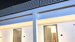 Un couloir d’hôtel avec deux portes en bois, une rambarde décorative en métal et un plancher de couleur claire.