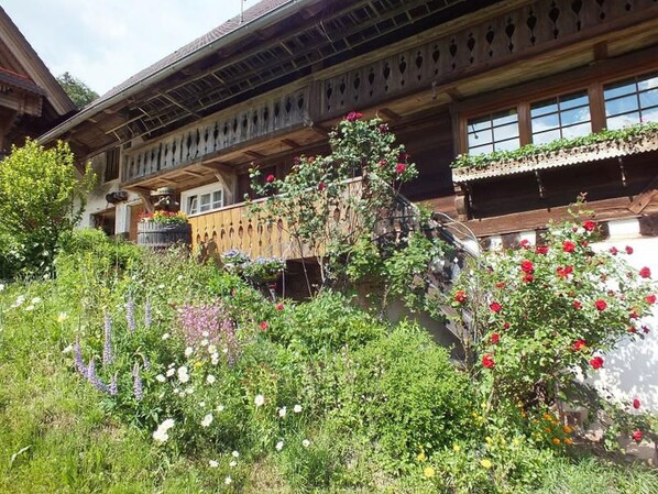 Un edificio de madera tradicional con balcones, rodeado de exuberante vegetación y diversas plantas florecientes.