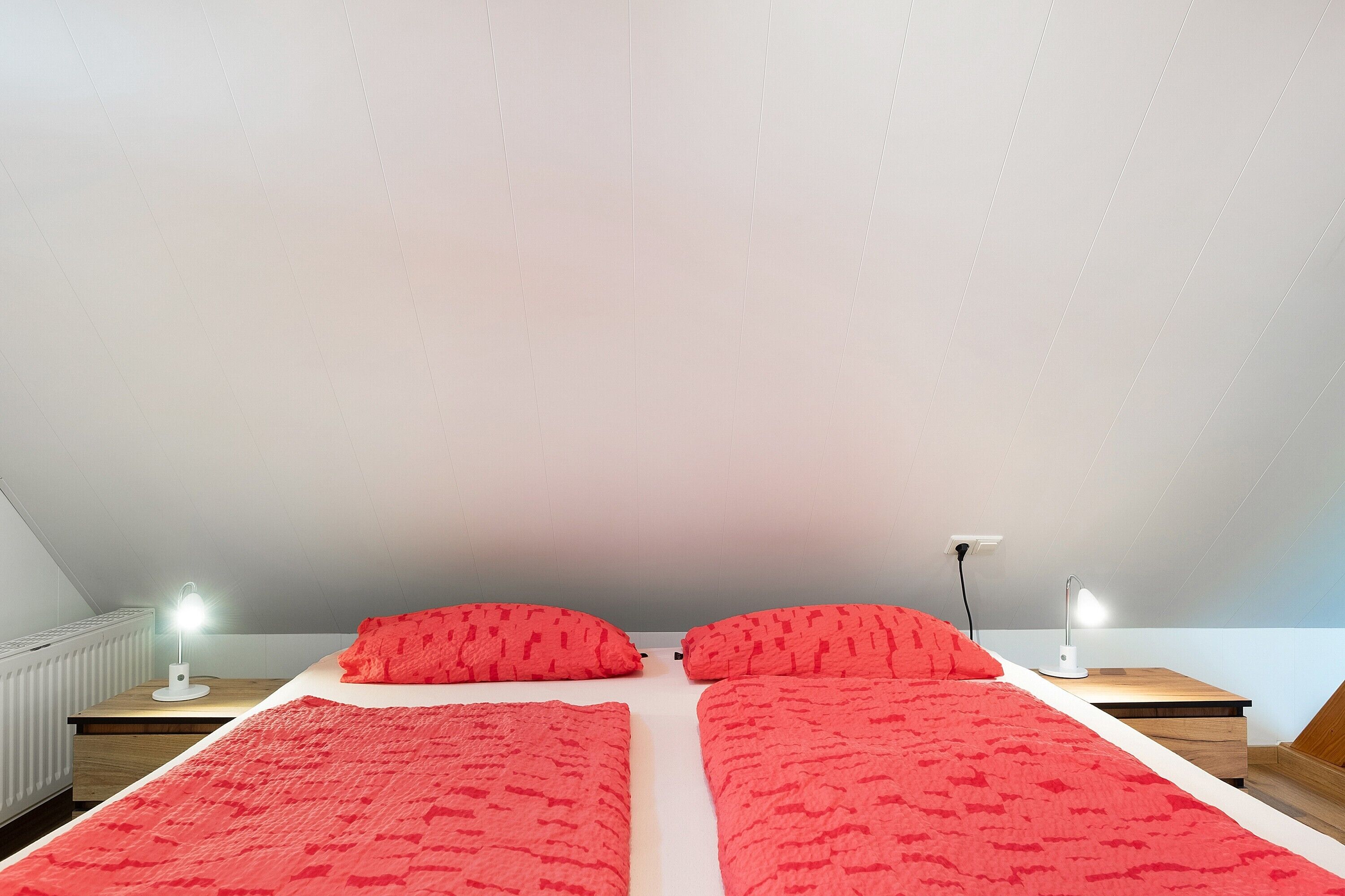 A bedroom with two beds, a nightstand with a lamp, and a radiator.