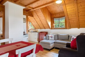 Una habitación acogedora con techo de madera, un sofá, una mesa de comedor con mantel rojo y una zona de cocina.
