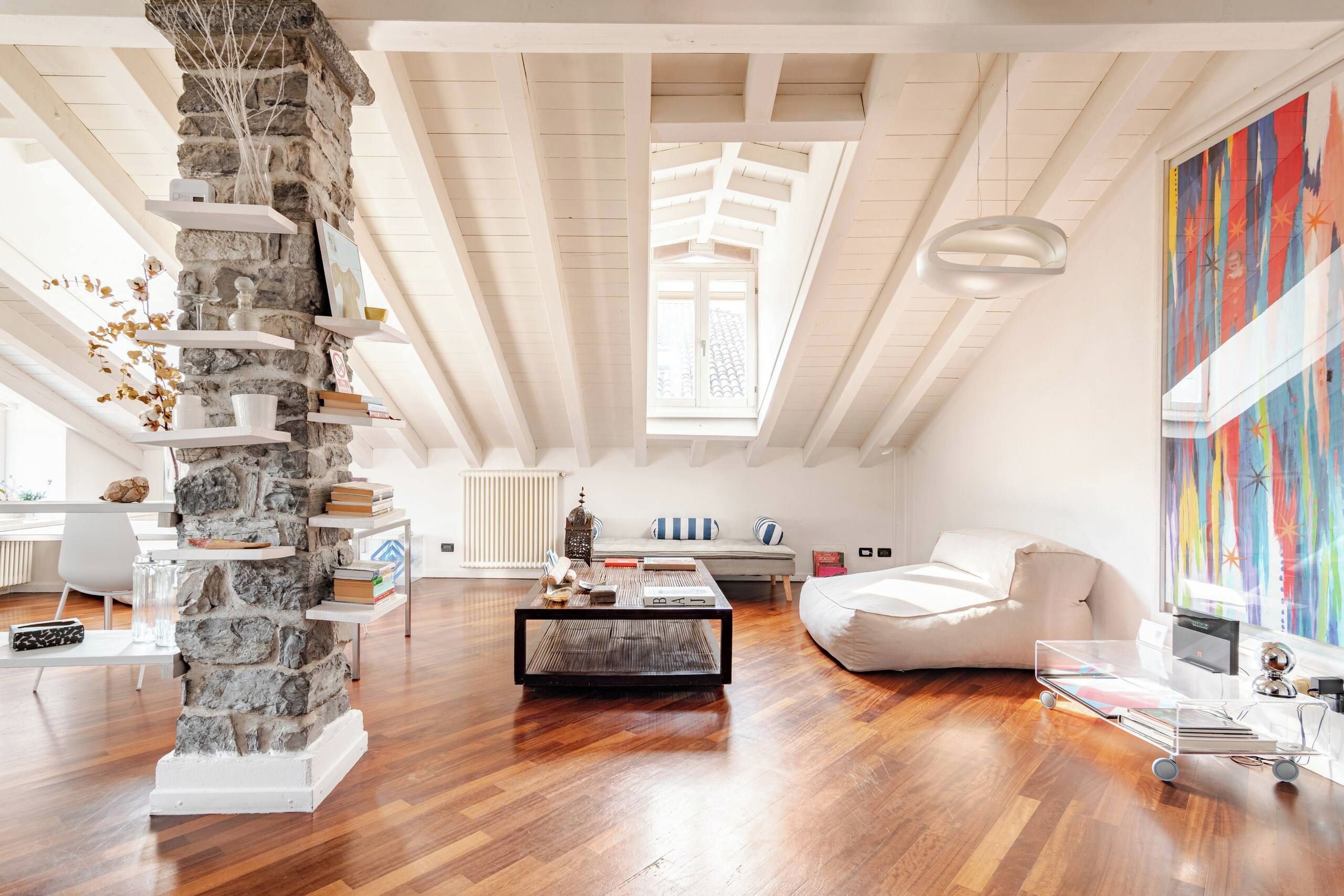 Spazioso loft con soffitti alti, una colonna in pietra, pavimento in legno, un divano bianco, un tavolino da caffè e un quadro astratto colorato.
