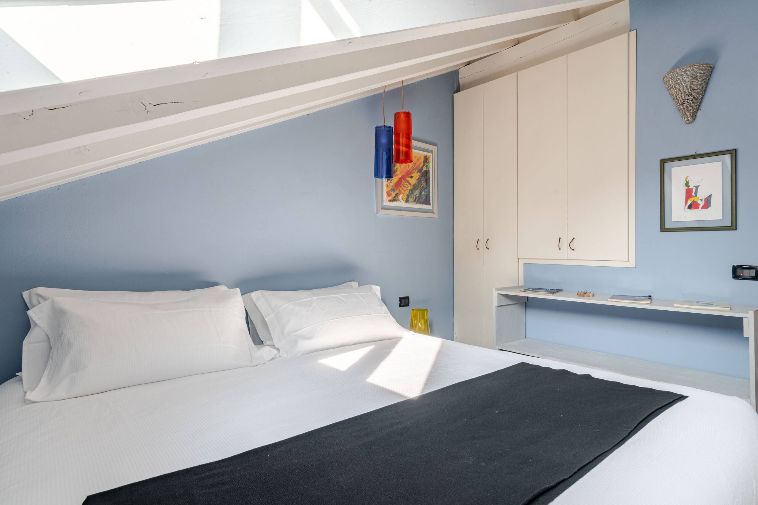 Una camera da letto con un letto, pareti bianche, un armadio bianco e opere d'arte appese al muro.
