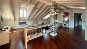 A modern loft with a high ceiling, exposed wooden beams, a stone column, and a long dining table. - Vanessa's Art Rooftop (Como)