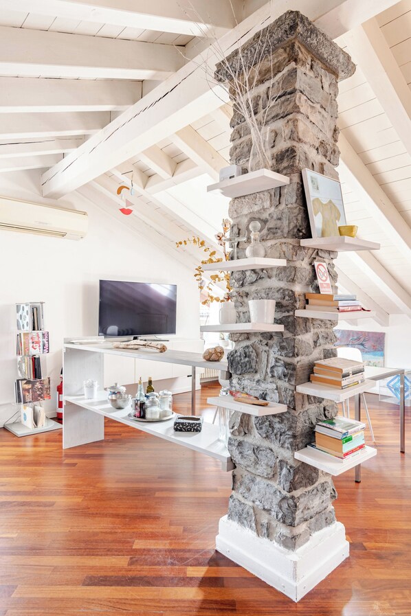 A modern interior with a stone column, white shelves, a flat-screen TV, and wooden flooring.