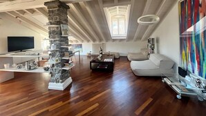 A spacious living area with a stone pillar, a television, a sofa, and a colorful abstract painting. - Vanessa's Art Rooftop (Como)