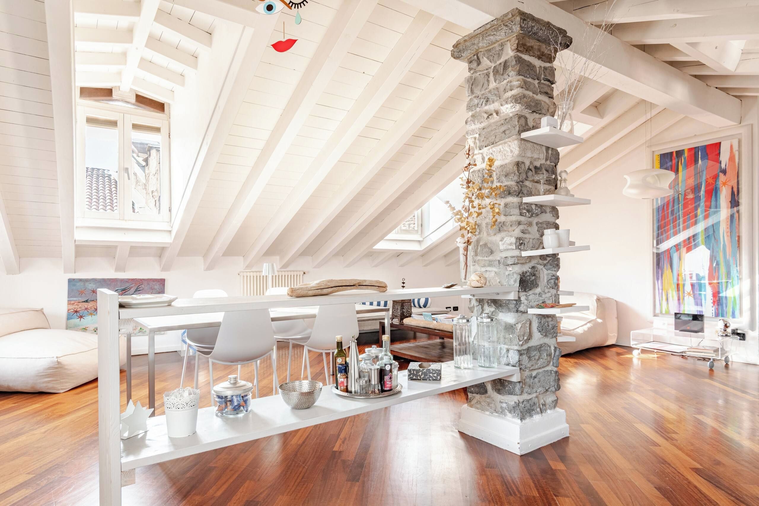 Un loft moderno con soffitto alto, travi a vista, un pilastro in pietra e un'area pranzo con un tavolo lungo e sedie.