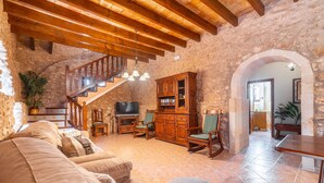 Un salón acogedor con pared de piedra, vigas de madera en el techo, un televisor, un mueble y una escalera.