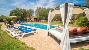 Un área junto a la piscina con sillones de descanso y una cama con dosel.