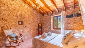 Una habitación con paredes de piedra, una cama, una mecedora y una ventana con cortinas.