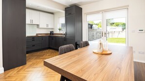 A modern kitchen with dark cabinets, a wooden dining table, and a sliding glass door leading to a backyard. - 3 Bed Home W/Garden By Phoenix Park & Dublin Zoo (Sublin 7)