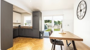 A modern kitchen with grey cabinets, a wooden herringbone floor, and a dining area with a wooden table and chairs. - 3 Bed Home W/Garden By Phoenix Park & Dublin Zoo (Sublin 7)