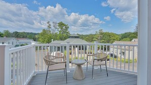 A covered outdoor area with two wicker chairs and a round table, overlooking a residential neighborhood with houses and trees. - Historical Housatonic Street apartment (Lenox)