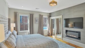 A modern bedroom with a large bed, a fireplace, and a TV mounted on the wall. - Historical Housatonic Street apartment (Lenox)
