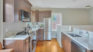 A modern kitchen with wooden cabinets, stainless steel appliances, and a large window. - Historical Housatonic Street apartment (Lenox)