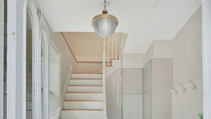 A staircase with white steps leading to a landing, a black doormat, and a white cabinet with a plant on top. - Historical Housatonic Street apartment (Lenox)
