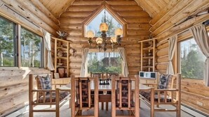 Interno di una baita in legno con un tavolo da pranzo, sedie, un lampadario e mensole piene di oggetti vari.