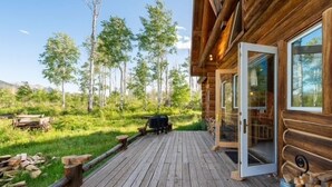 Una baita di legno con una veranda, un ingresso con porta in vetro e vista su una zona boschiva.