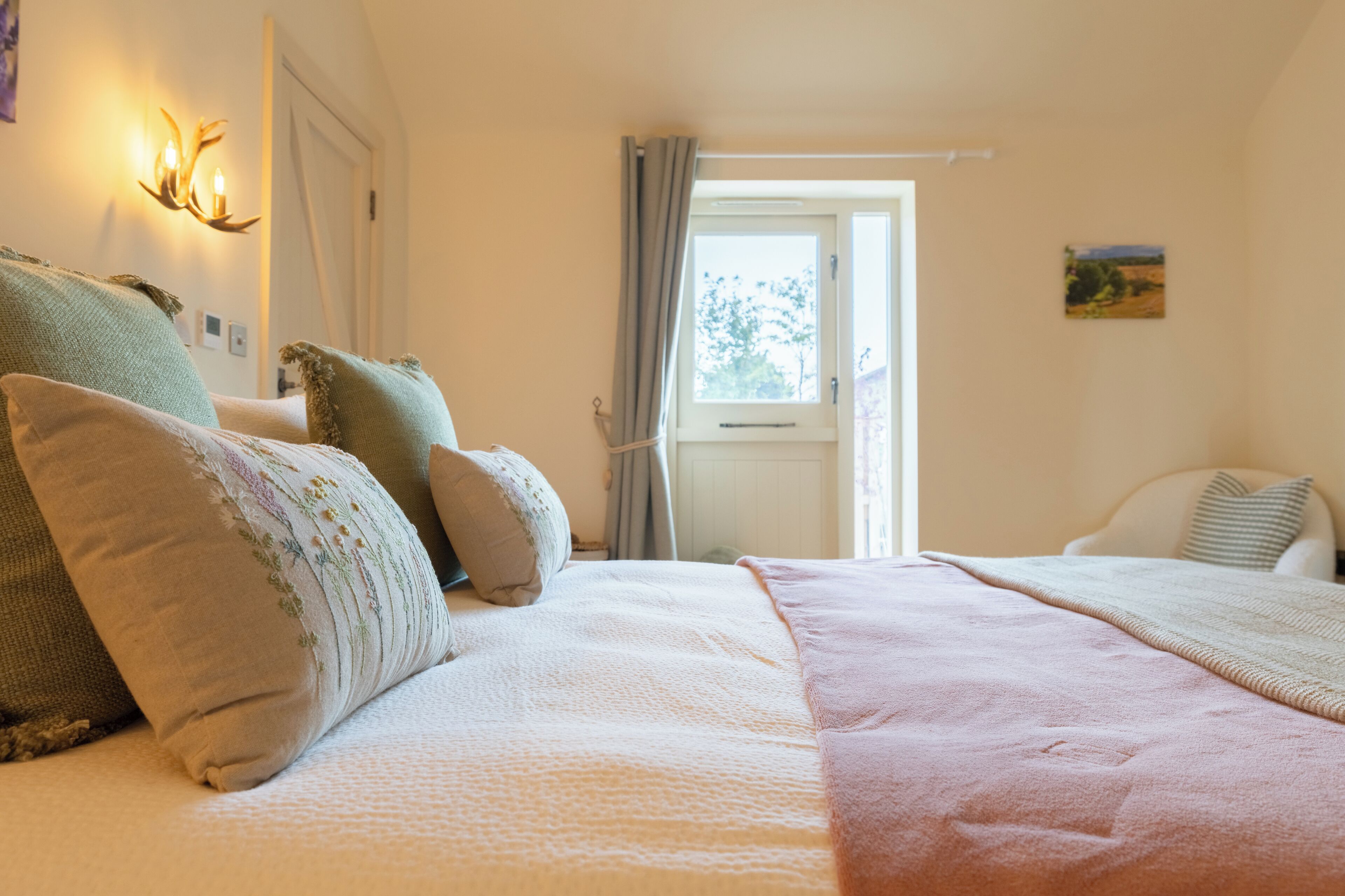 Un dormitorio con una cama grande, una ventana con cortinas y una lámpara fijada a la pared.