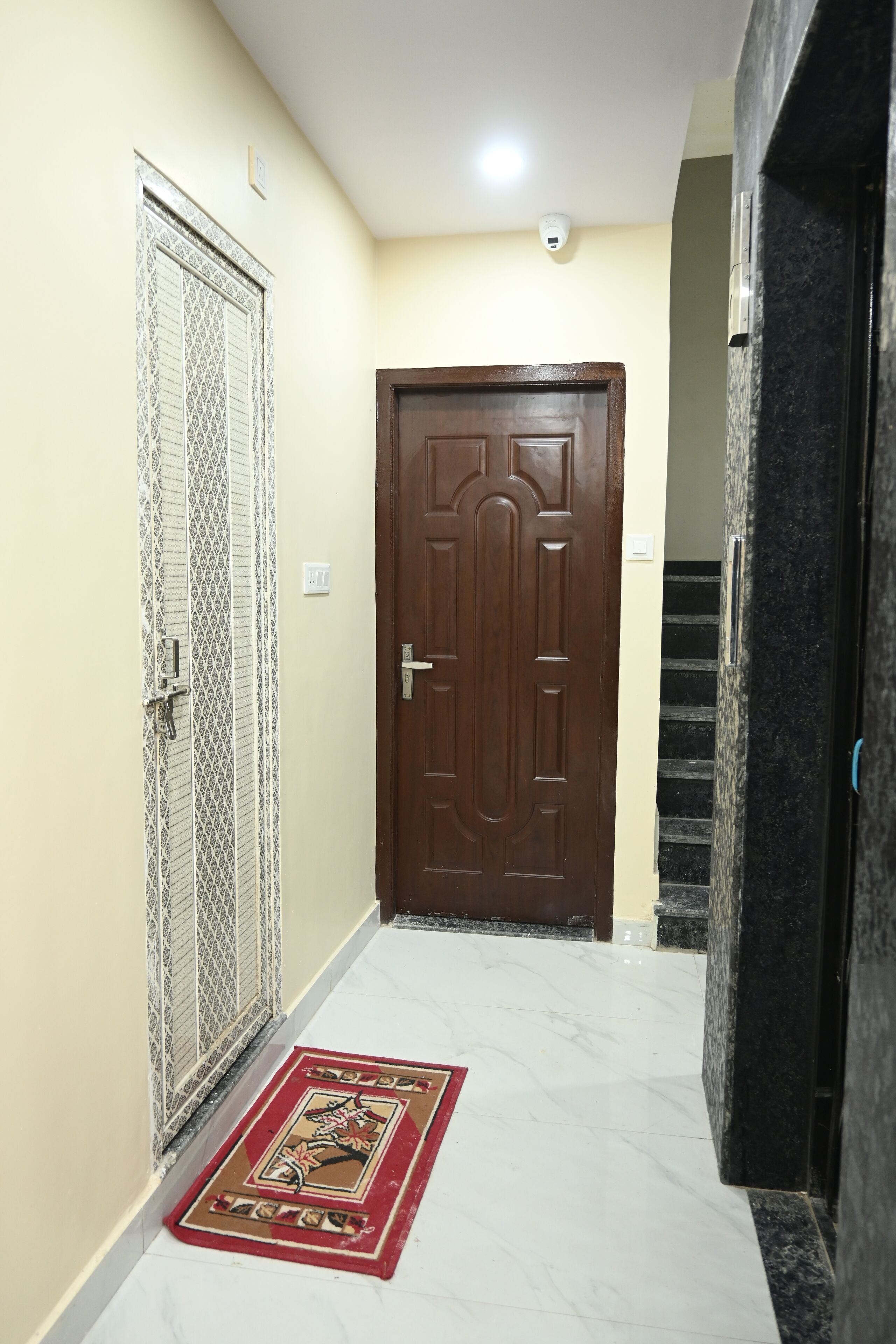 A hallway with a wooden door, a metal gate, and a red doormat.