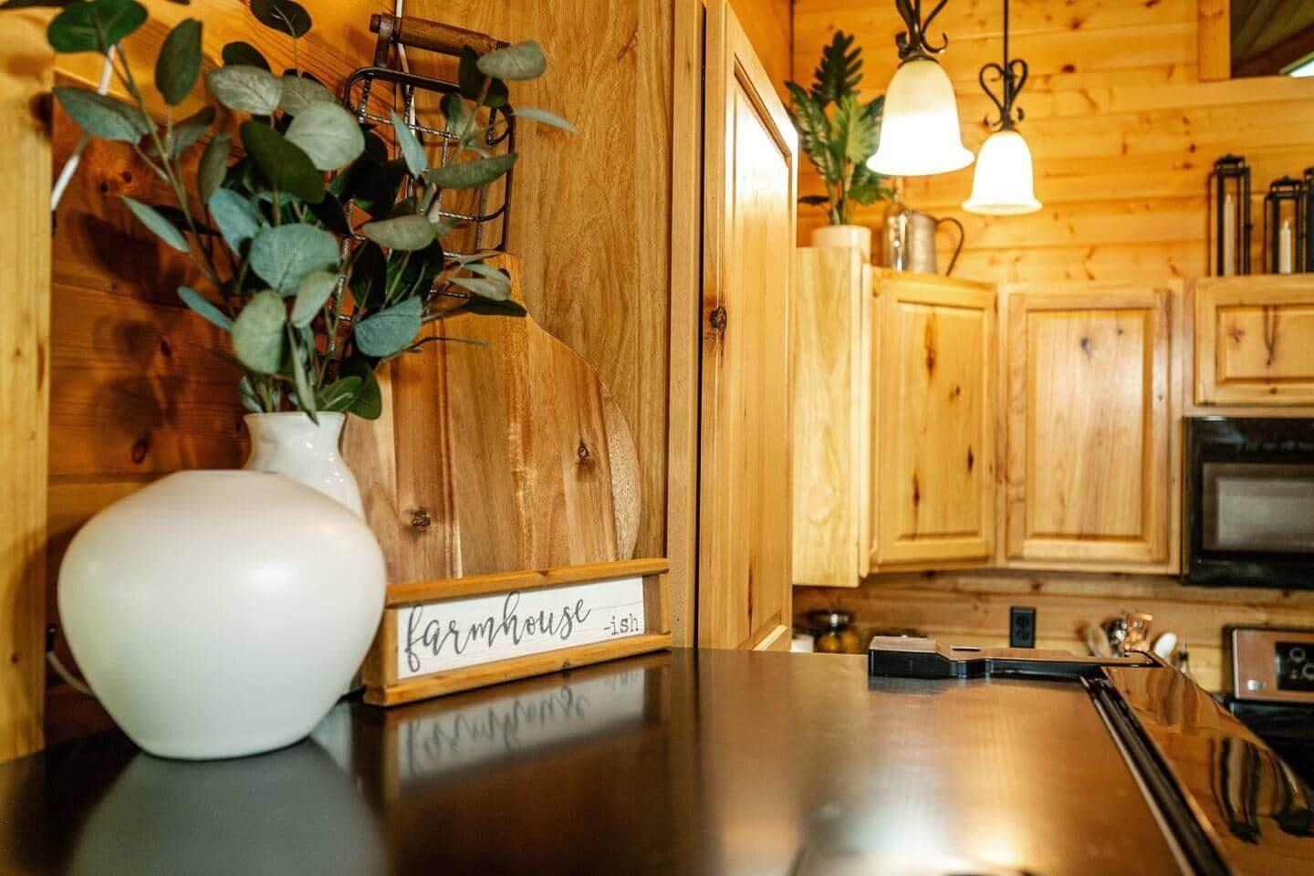 Una cocina rústica con armarios de madera, un florero blanco con plantas verdes y un letrero que dice 'farmhouse-ish'.