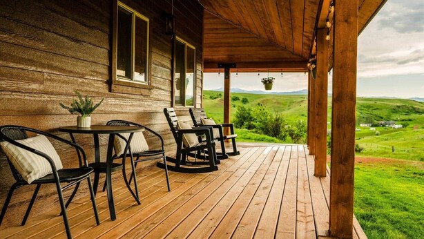 Eine Holzveranda mit Sitzgelegenheiten im Freien, einer hängenden Pflanze und Blick auf eine grüne Landschaft.