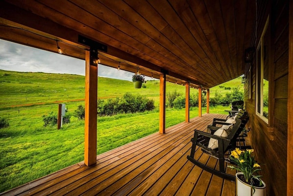 A wooden deck with outdoor seating, a hanging planter, and a view of a green field.