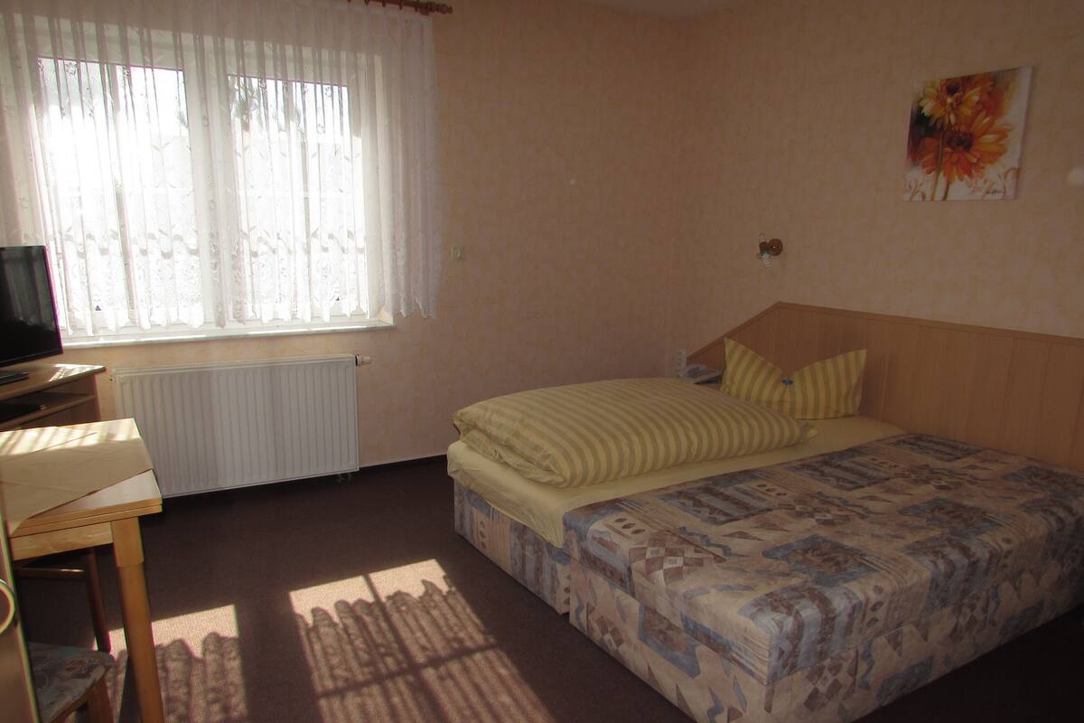 A bedroom with a bed, a desk, a radiator, and a window with curtains.