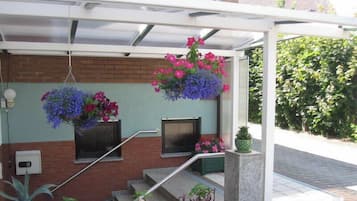 Ein überdachter Außenbereich mit hängenden Blumenkörben und einer Treppe, die zu einer Backsteinmauer führt.