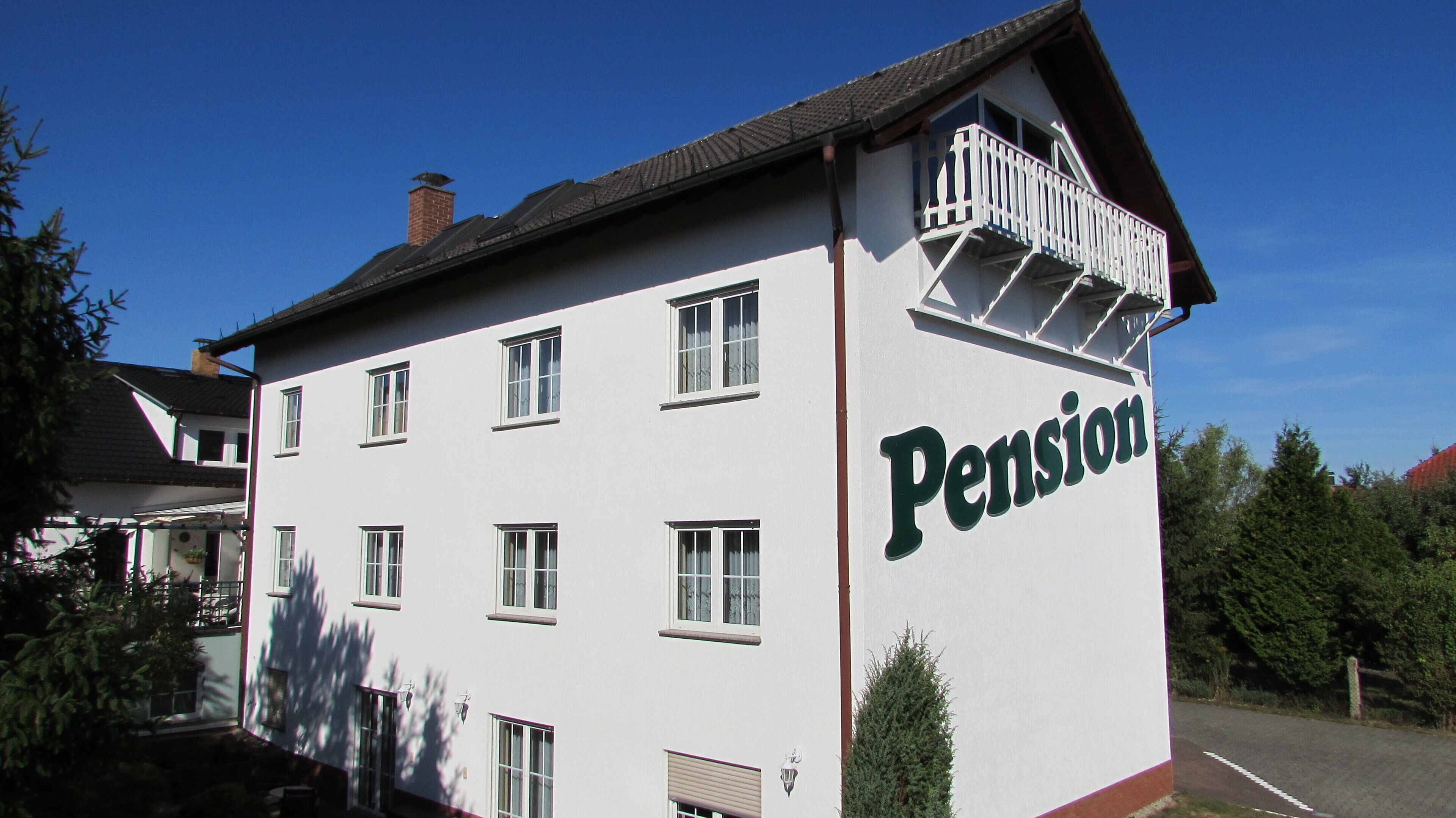 Ein weißes Gebäude mit dem Schriftzug "Pension", zahlreichen Fenstern und einem Balkon.
